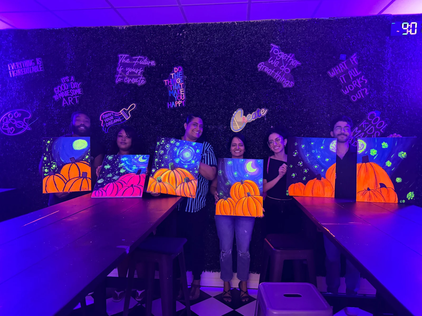 Six Studio 786 guests showing their glowing pumpkin paintings under UV lights