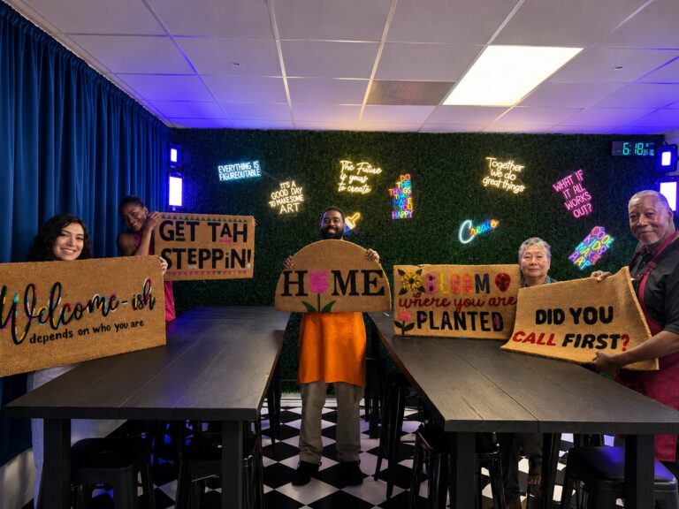 Guests holding personalized painted doormats beneath the LED art wall at Studio 786 in Houston