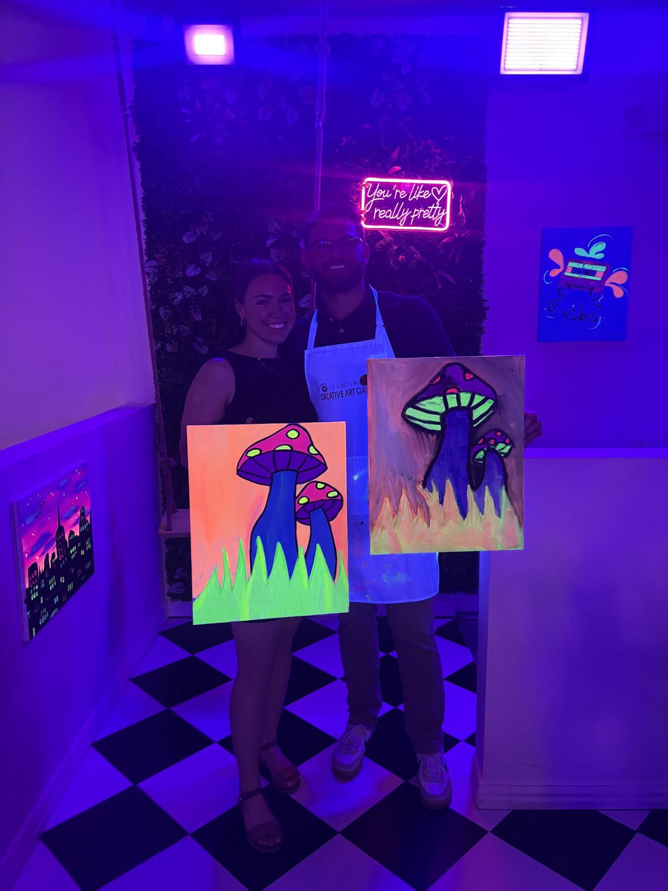 Couple displaying finished neon mushroom paintings under black lights at Studio 786 Houston