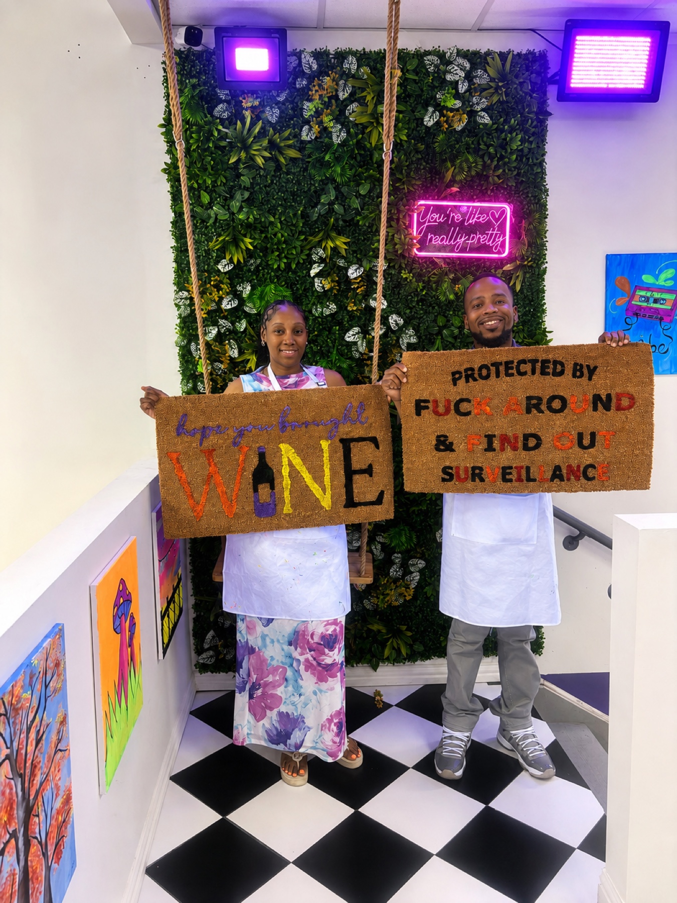 Two guests holding custom painted doormats under LED lights at Studio 786 in Houston
