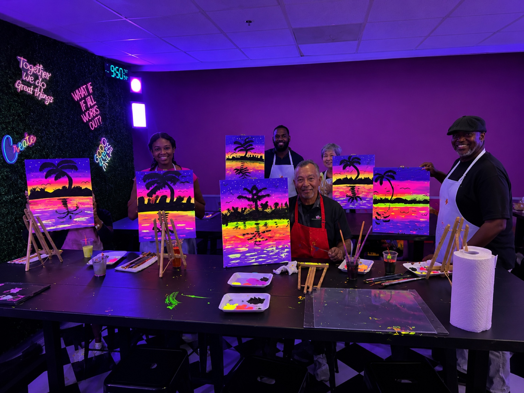 Group displaying colorful sunset paintings after a UV glow painting class at Studio 786 Houston