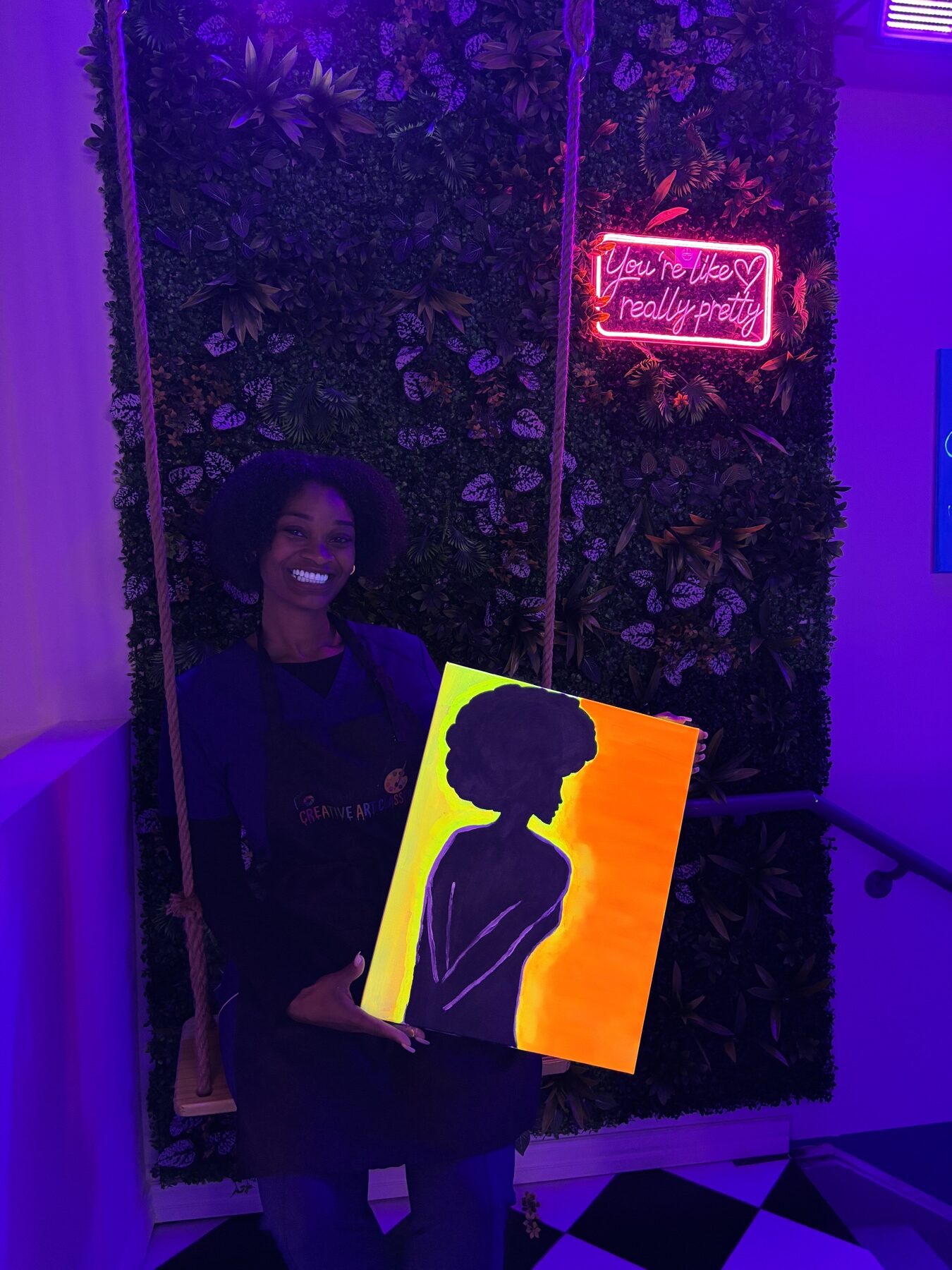 Guest displaying a bright orange and yellow portrait painting under UV lights at Studio 786 Houston