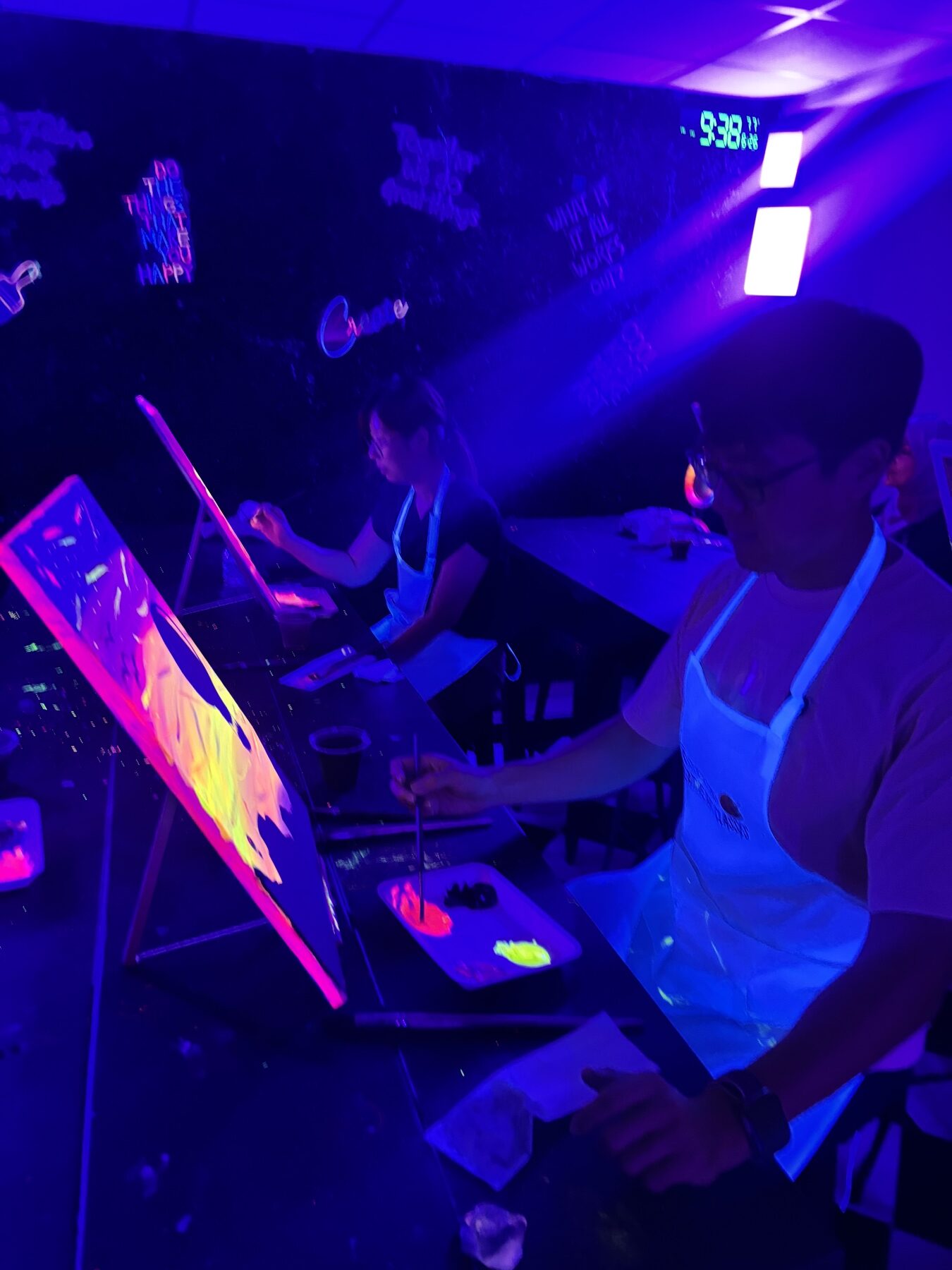 Guest painting a bright neon canvas during a UV glow painting class in Houston