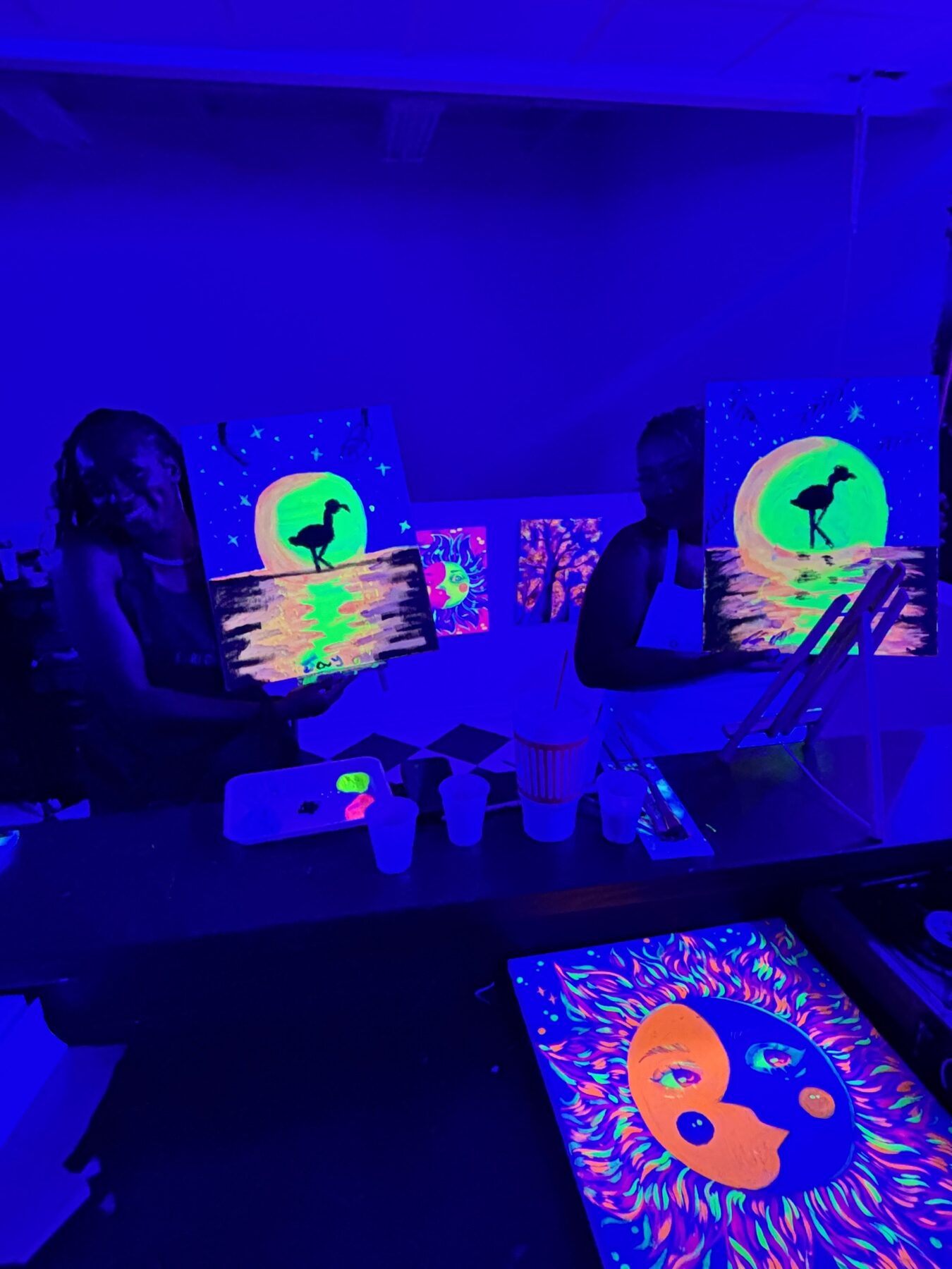 Guests displaying colorful flamingo and sun paintings during a Studio 786 UV class