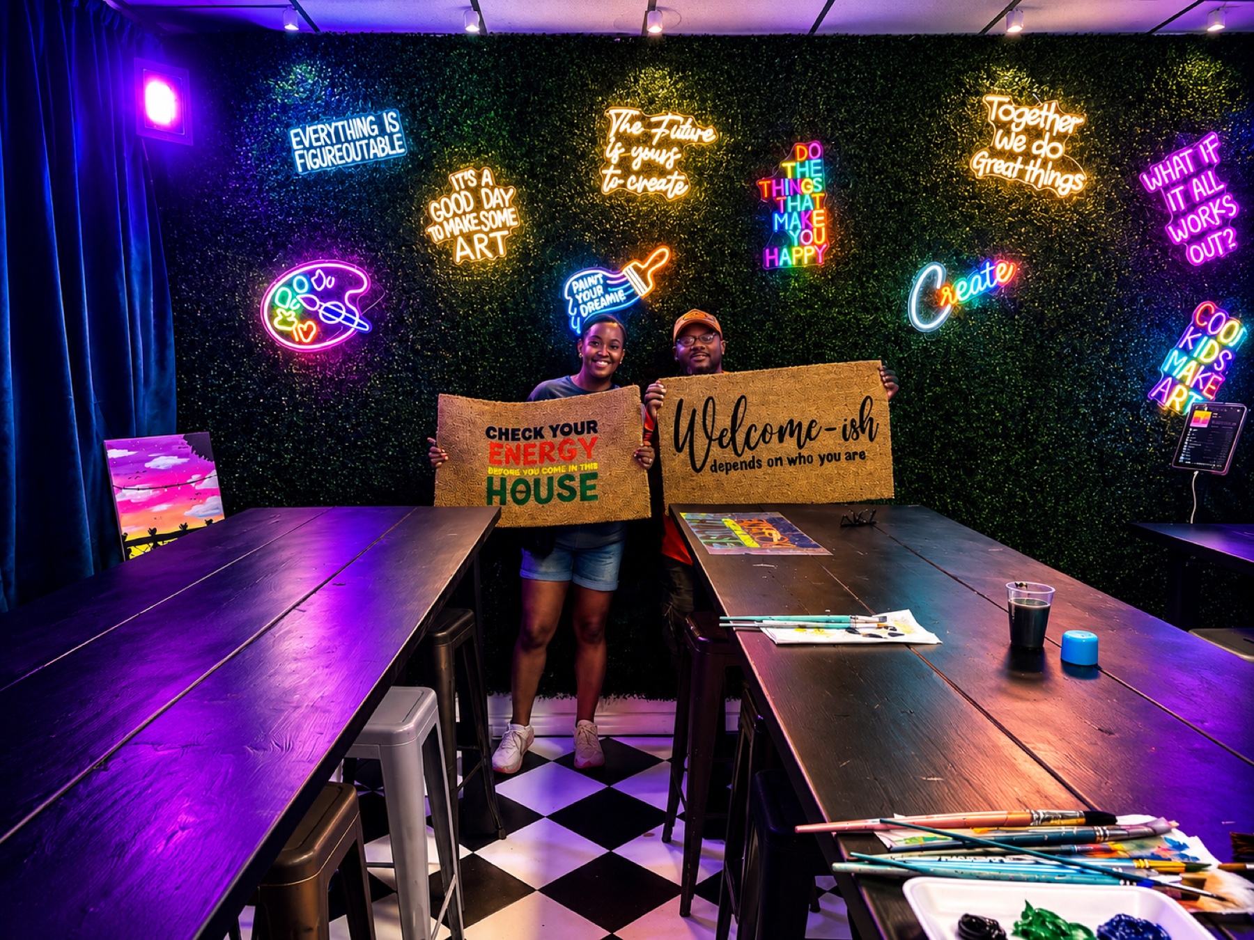 Guests holding finished painted doormats under colorful LED lights at Studio 786 Houston