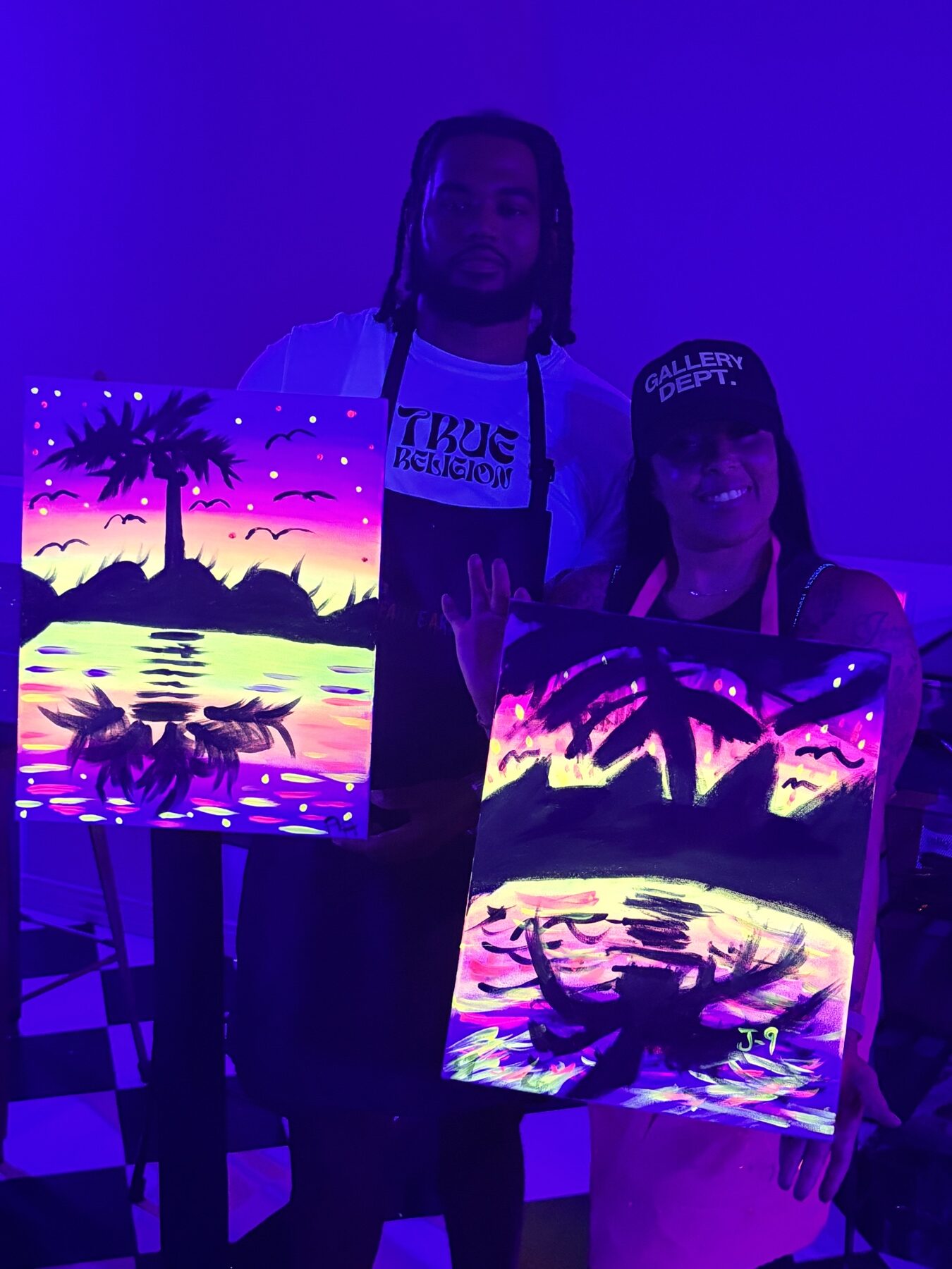 Guests displaying finished neon paintings during a UV glow painting class at Studio 786 Houston