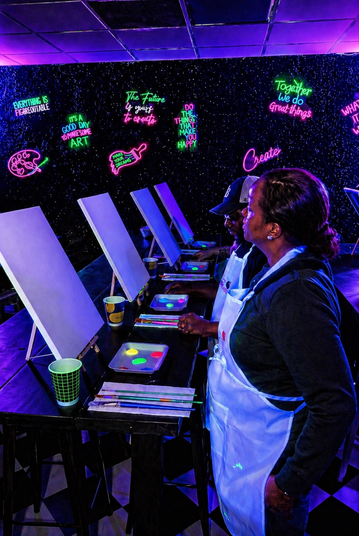 Guests seated at easels with neon paint ready for a UV glow painting class in Houston