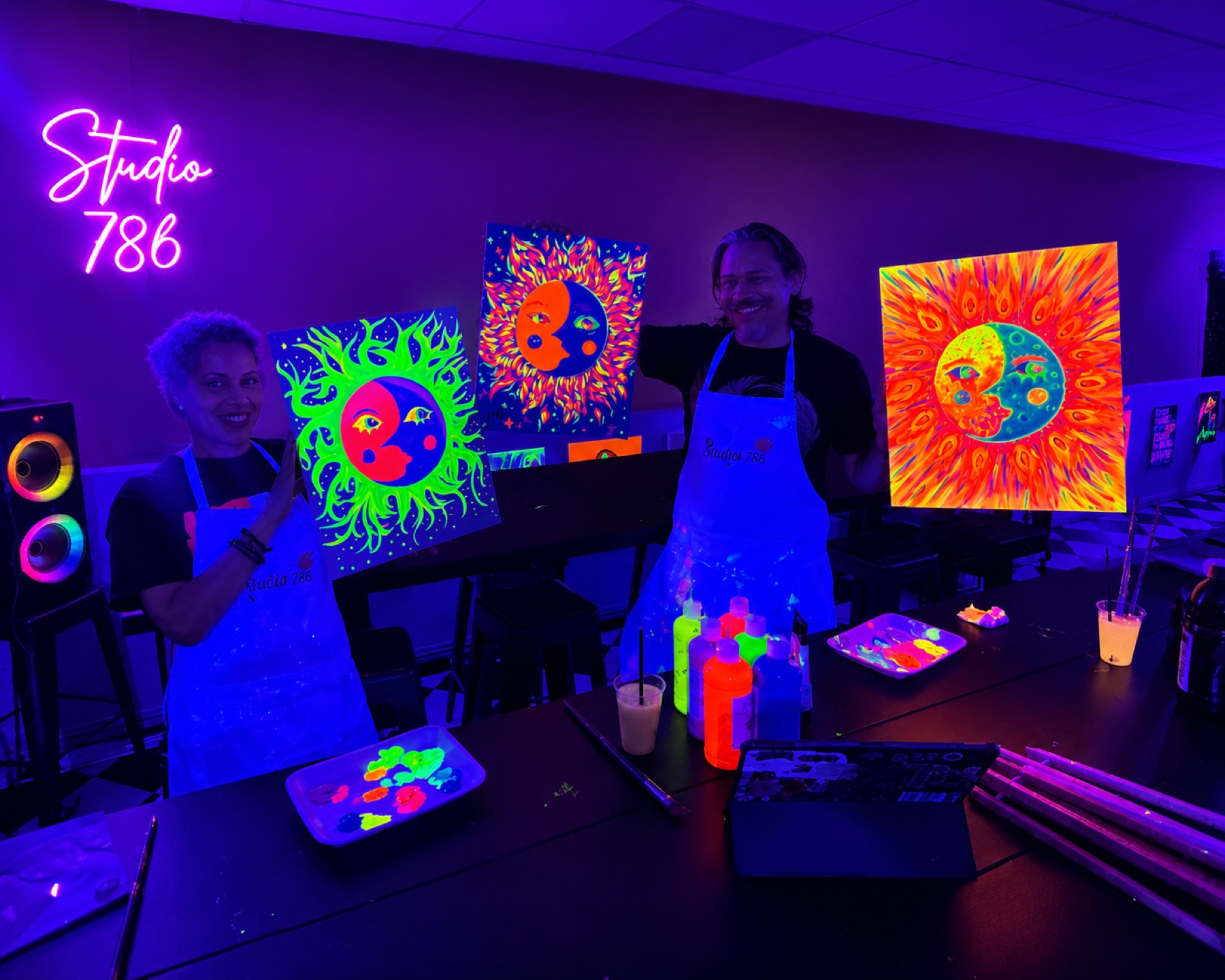 Guests holding vivid sun and moon paintings under black lights at Studio 786 Houston