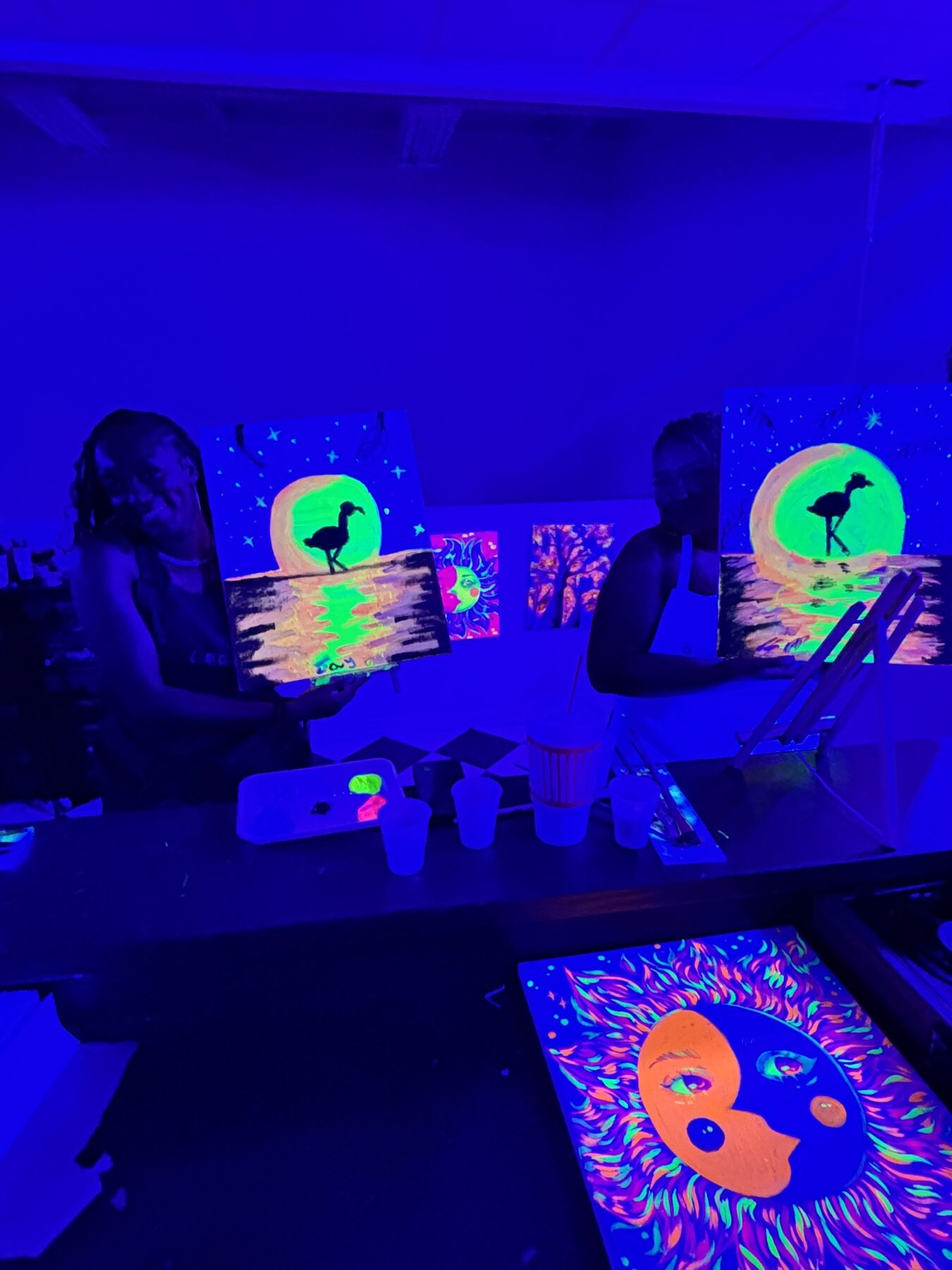 Finished glow paintings and guests inside the Studio 786 black-light art studio